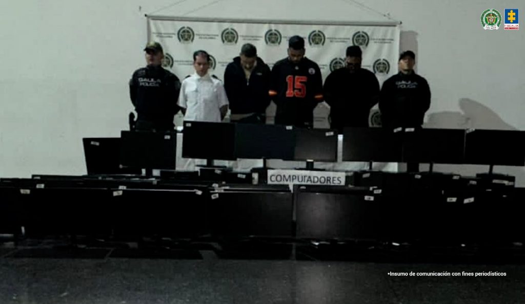 En la imagen están los 4 procesados con dos servidores de la Policía Nacional y en la parte de adelante están ubicadas las 48 pantallas de computador incautadas