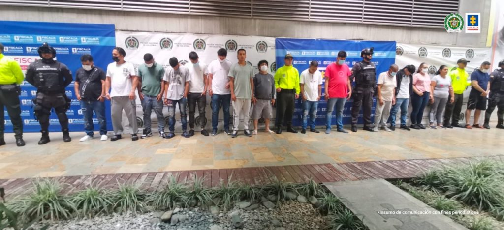 En la imagen hay 15 capturados de frente con funcionarios del CTI Y la Policía Nacional, con la imagen pendones de ambas instituciones al fondo