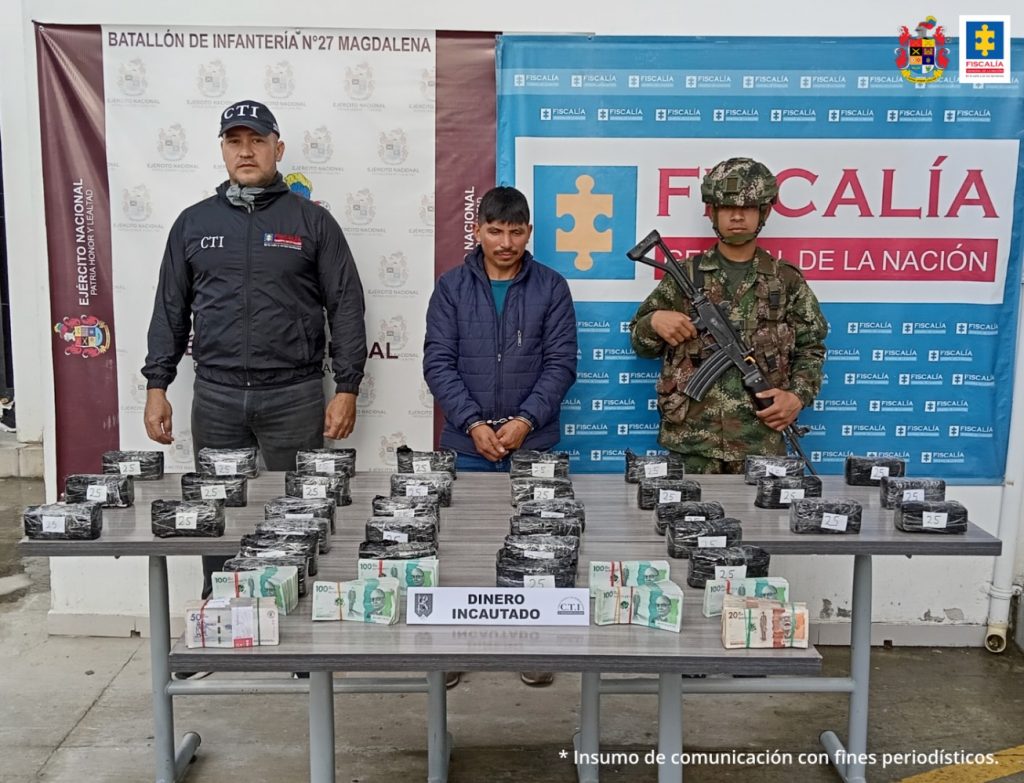 En la imagen se observa al frente una mesa con el dinero incautado, luego a un agente del CTI en el costado izquierdo y al derecho un militar; y en medio Robier Afranio López, capturado en flagrancia transportando el dinero, cuya procedencia no justificó. Al fondo de la imagen un cartel de la Fiscalía General de la Nación.