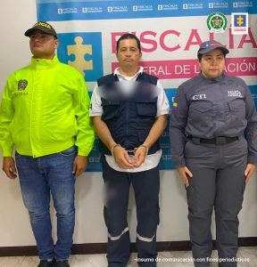 En la fotografía se ve al detenido al lado de un oficial de la policía y un miembro del CTI, de fondo un backing de la Fiscalía General.