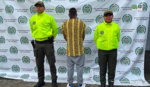El capturado aparece de espalda a la cámara, en medio de dos uniformados de la Policía y con sus manos esposadas.