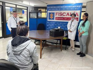 dos Funcionarias del CTI explican el protocolo. Atrás un pendón de la Fiscalía General de la Nación. Adelante una mesa con la Urna funeraria.