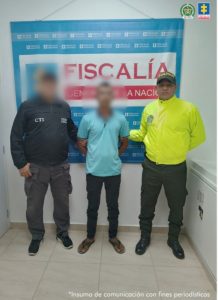 En la imagen se observa al detenido en compañía de un uniformado del CTI y un unofrmado de la Policía Nacional. De fondo se observa un pendón de la Fiscalía. Los rostros de los hombres aparece borroso