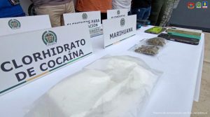 En una mesa aparecen los elementos incautados como armas, celulares estupefacientes y de fondo, están los capturados esposados y custodiados por uniformados de la Policía Nacional.