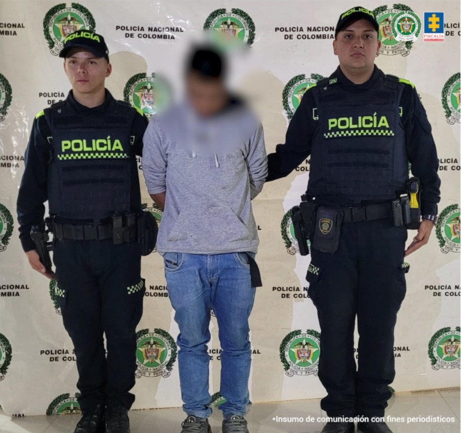 en la fotografia se puede ver al capturado con su rostro borroso en medio de dos policias y detras de ellos hay un baking de la policia