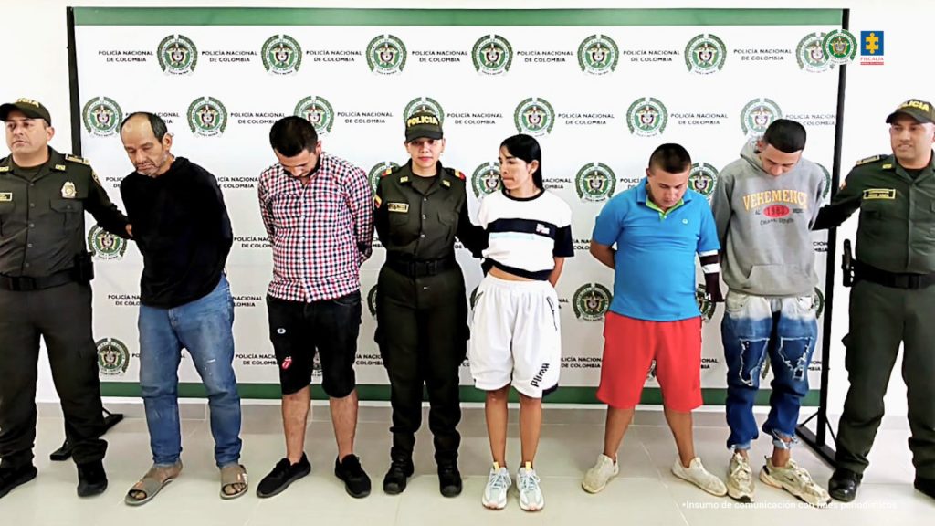 Los procesados aparecen custodiados por uniformados de la Policía nacional, esposados y de fondo un pendón institucional.