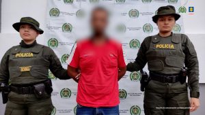 El procesado se encuentra esposado y en custodia por uniformados de la Policía Nacional. Detrás suyo un backing de la Policía.