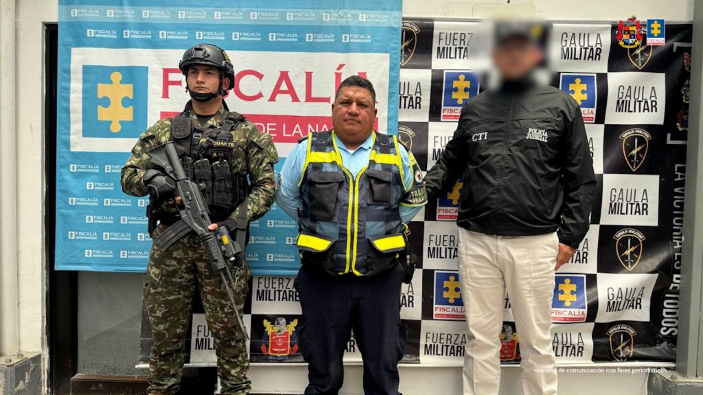 El capturado aparece con su uniforme de agente de tránsito, esposado y custodiado por un servidor del CTI de la fiscalía y un uniformado del ejército nacional.