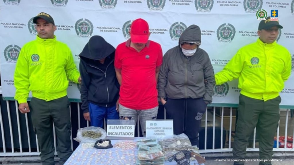 se observan los tres capturados de frente y en fila. A los costados funcionarios de Policía nacional custodiándolos, atrás un pendón de Policía Nacional y adelante una mesa con material incautado.
