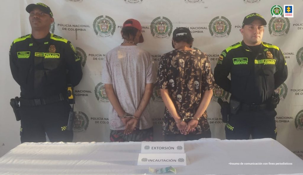 AL CENTRO SE OBSERVAN DOS CAPTURADOS. EN CADA COSTADO UNIFORMADOS DE POLICIA NACIONAL Y AL FONDO UN PENDÓN DE POLICÍA NACIONAL