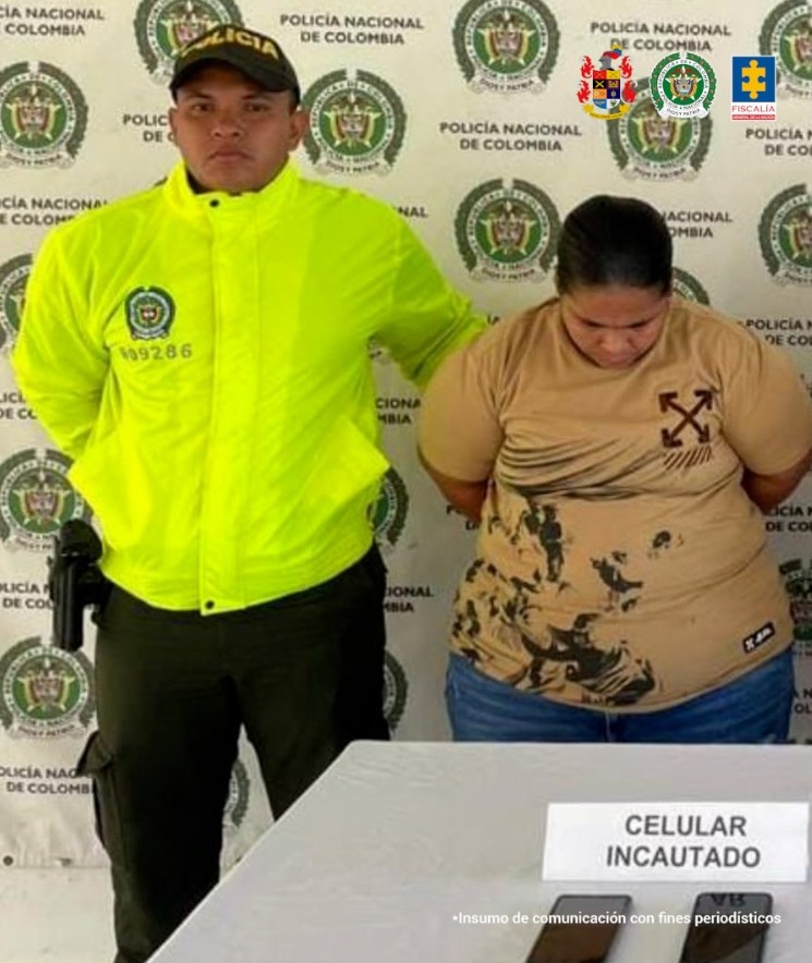 En la foto está la procesada con un servidor de La Policía Nacional y una mesa al frente con dos celulares incautados