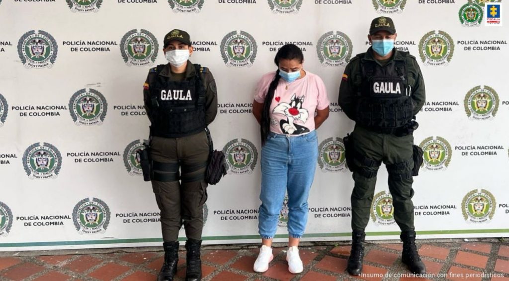 se observa una mujer capturada y a cada costado un funcionario de Policía Nacional.  Atrás un pendón de Policía Nacional
