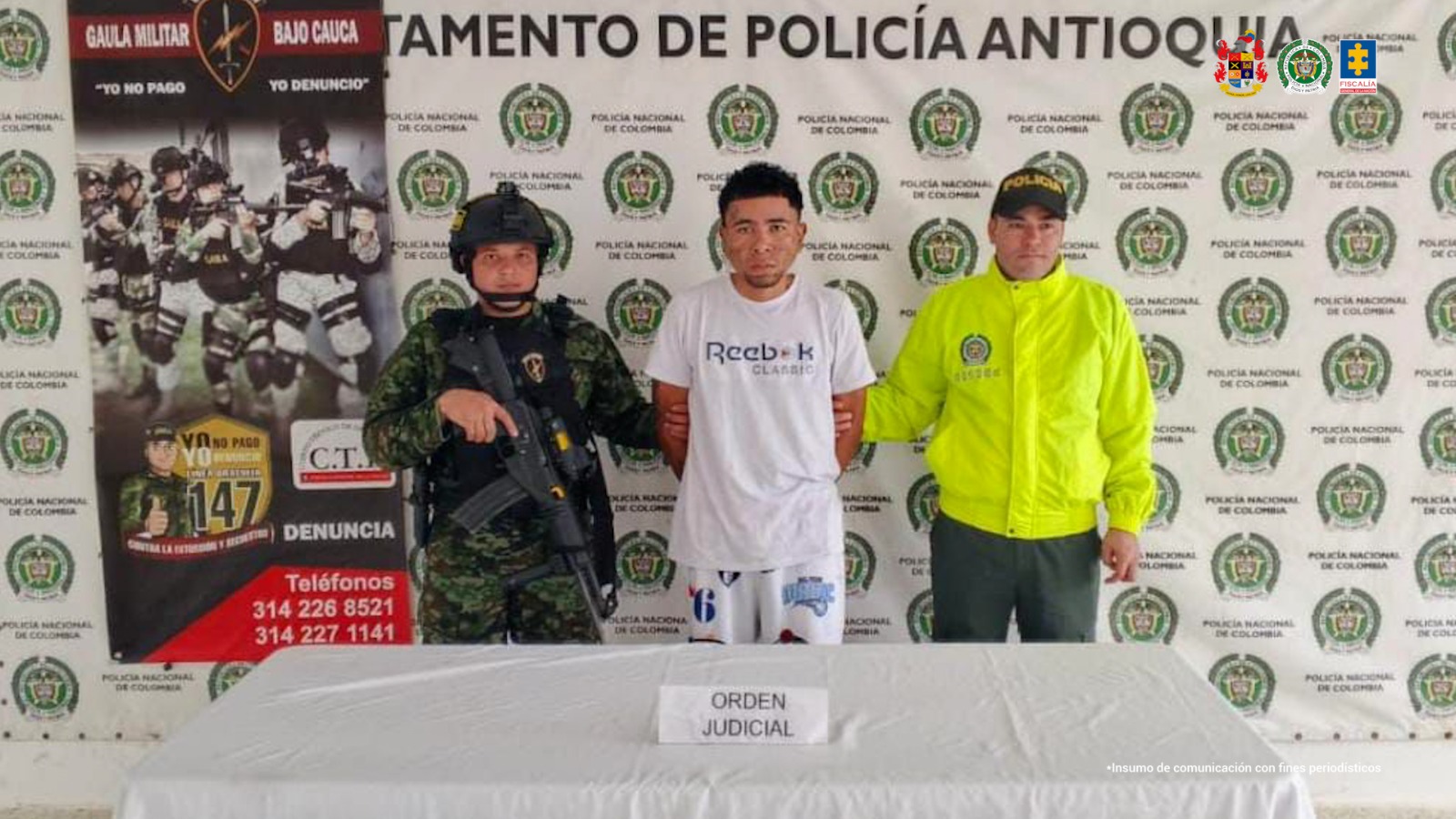 En la imagen aparece una persona de suéter blanco, entre un uniformado de la Policía y otro del Ejército.