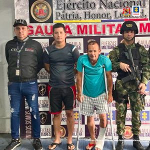 capturados de frente custodiados por un investigador del CTI de la fiscalía y por un militar. Detrás banner de Gaula Militar.