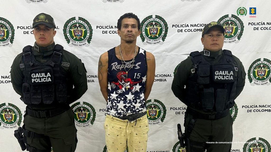 En la imagen sale una persona de camisilla negra y bermuda amarilla, entre dos uniformados de la Policía Nacional. 