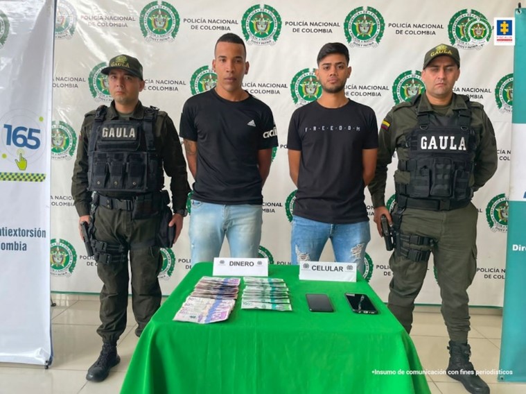 En la imagen se observan los dos capturados junto a uniformados del Gaula de la Policía Nacional, al frente de ellos una mesa con los elementos incautados dinero y teléfonos celulares. En la parte posterior se aprecia el banner de la Policía Nacional