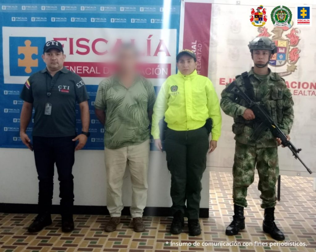 En las fotografía aparece un capturado, junto a personal de CTI, Policía Nacional y Ejército Nacional. En la parte posterior de la imagen se ven banners de Ejército Nacional, Policía Nacional y la Fiscalía General de la Nación.
