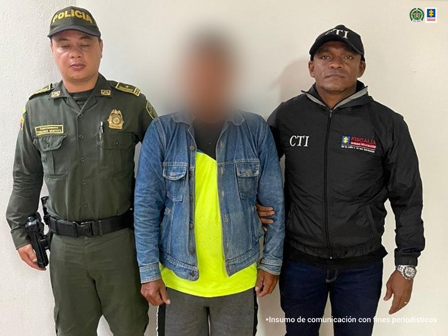 En la fotografía se aprecia de pie al hombre que habría abusado sexualmente de su nieta. Al lado derecho de él hay un uniformado de la Policía Nacional. Viste chaqueta de jean azul de manga larga y debajo de ella una camiseta amarilla con negro en la parte superior; bermuda gris y zapatos negros. Al lado izquierdo un servidor del CTI de la Fiscalía.