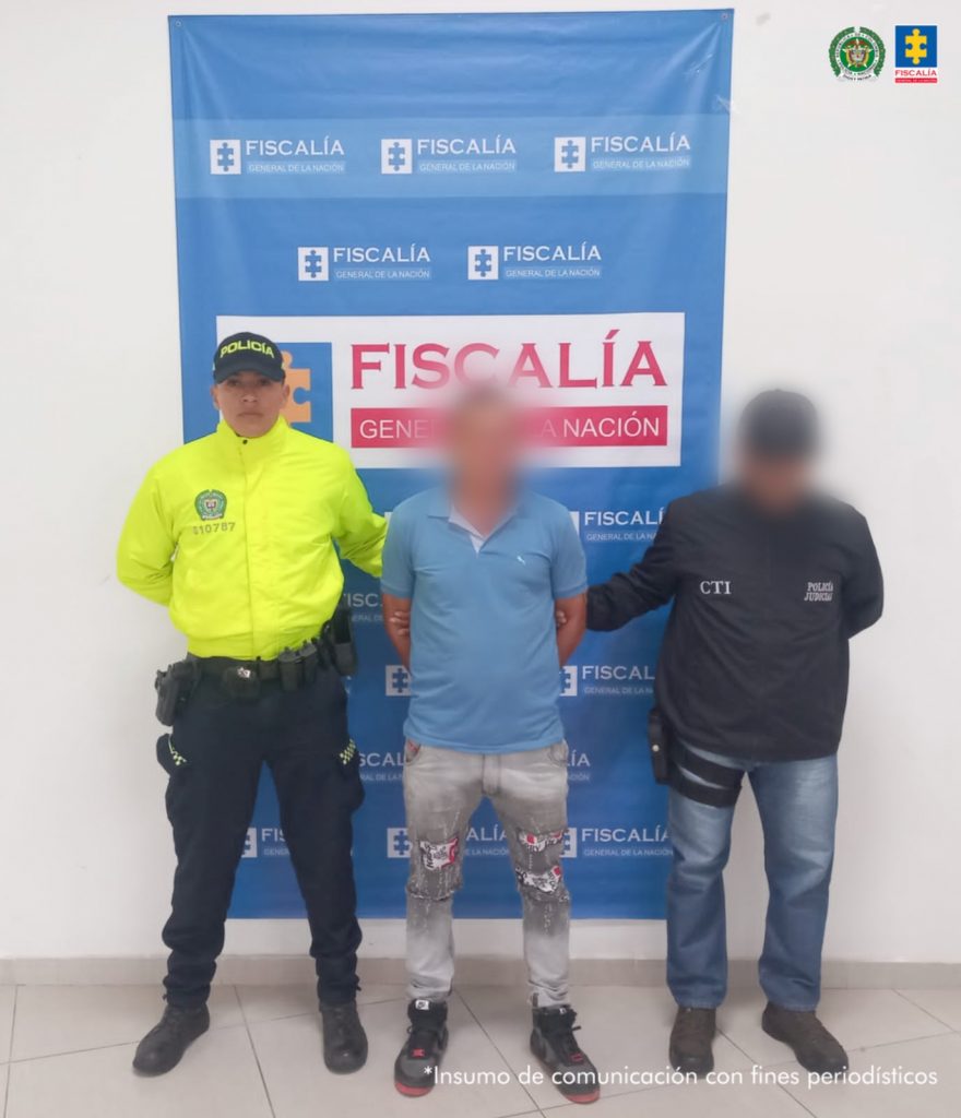 Se observa al capturado de frente, con un efecto que cubre su rostro. A un costado, un funcionario del CTI y al otro, uno de Policías Nacional. Atrás, un pendón de Fiscalía General de la Nación