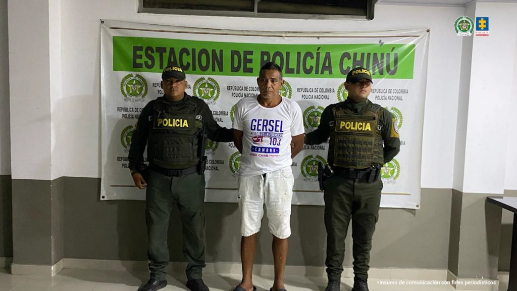 En la imagen aparece una persona de bermuda blanca y camiseta blanca, entre dos uniformados de la Policía.