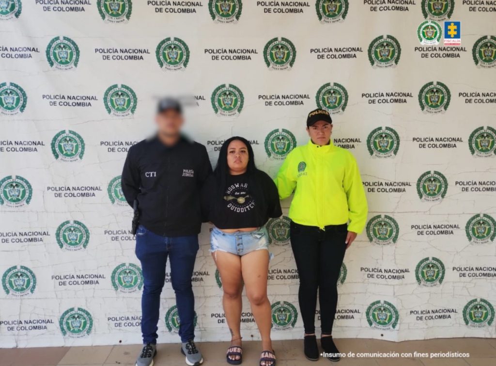 En la fotografía aparece de pie y con los brazos atrás Adriana Margarita Licona Iglesia. Viste con blusa corta de color negro, con estampado circular de color gris; pantalón corte de jean y pantuflas. Al extremo derecho de ella hay un servidor del CTI de la Fiscalía y al izquierdo una uniformada de la Policía Nacional. Detrás de ellos hay un pendón institucional de la Policía.