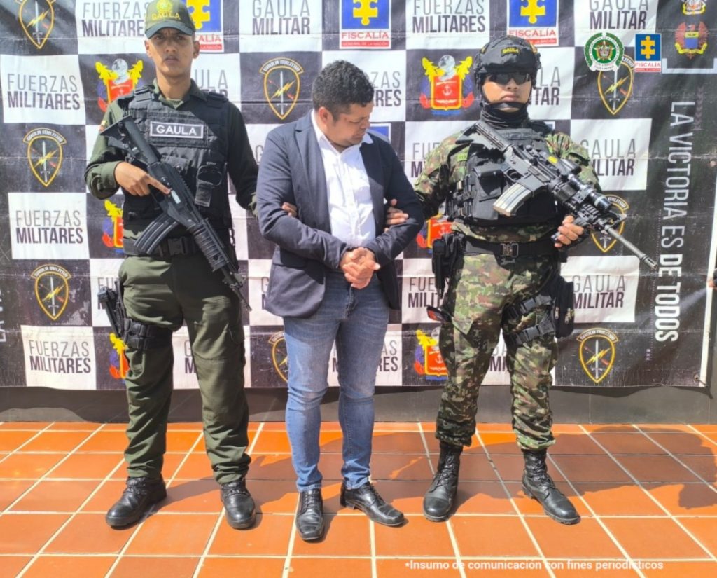 Se observa al agente de tránsito en custodia por dos uniformados del Gaula de la Policía Nacional. Detrás se observa un backing de la Policía