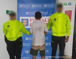 Se observa al capturado junto a dos uniformados de la Policía Nacional. En la parte posterior se ubica el banner que identifica a la Fiscalía General de la Nación