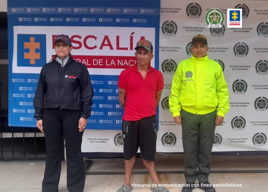 En la fotografía aparece un capturado, junto a personal de Policía Nacional y Fiscalía General de la Nación. En la parte posterior de la imagen se ven banners de Policía Nacional y la Fiscalía General de la Nación.