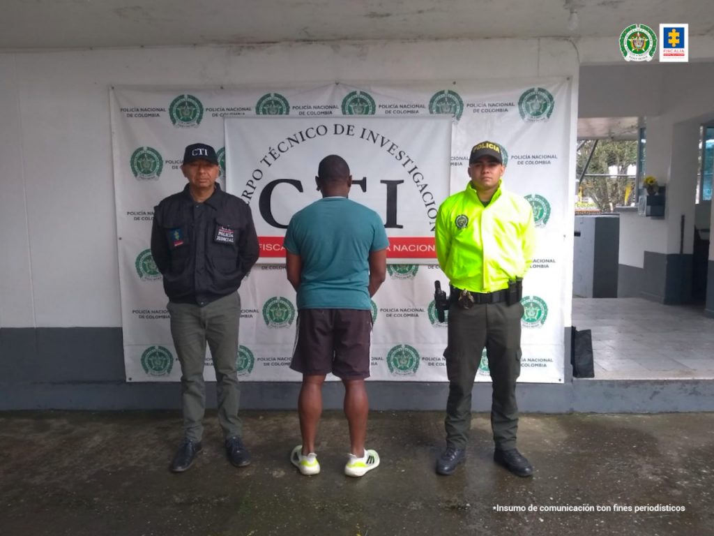 En la foto aparece de espalda, Albeiro Viáfara Castillo. Viste bermuda negra, camiseta verde de manga corta y tenis blancos con rayas negras. Al lado izquierdo de él hay un servidor del CTI de la Fiscalía y a su derecha un uniformado de la Policía Nacional. En la parte posterior, hay dos pendones institucionales de la Policía y del CTI.