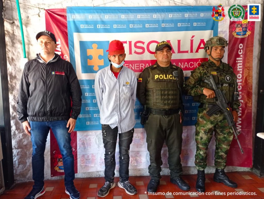 En la fotografía aparece un capturado, junto a personal de CTI, Policía Nacional y Ejército Nacional. En la parte posterior de la imagen se ven banners de Ejército Nacional, Policía Nacional y la Fiscalía General de la Nación.