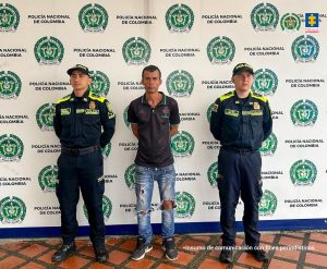 se observa al capturado de frente y a cada costado un funcionario de Policía Nacional, atrás, un pendón de Policía Nacional