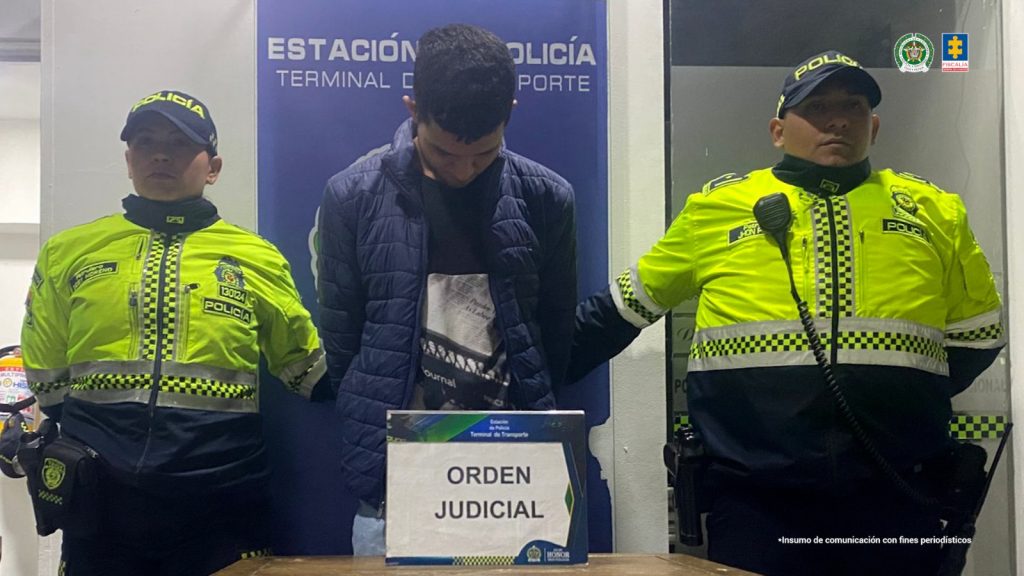 En la fotografía aparece un hombre capturado, acompañado por dos uniformados de La Policía Nacional. En la parte posterior un banner con logos de la entidad.