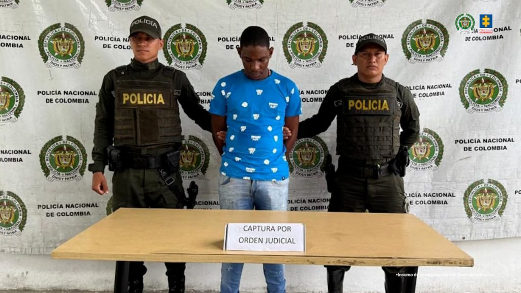En la fotografía aparece el capturado junto a dos uniformados de la Policía Nacional. En la parte superior está un banner de la Policía Nacional.