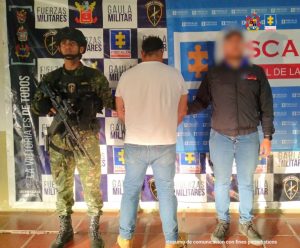 El capturado se encuentra de espaldas y en custodia de un servidor del Cuerpo Técnico de Investigación CTI y un uniformado del Gaula del Ejército Nacional. Detrás hay un backing de la Fiscalía y el Ejército.