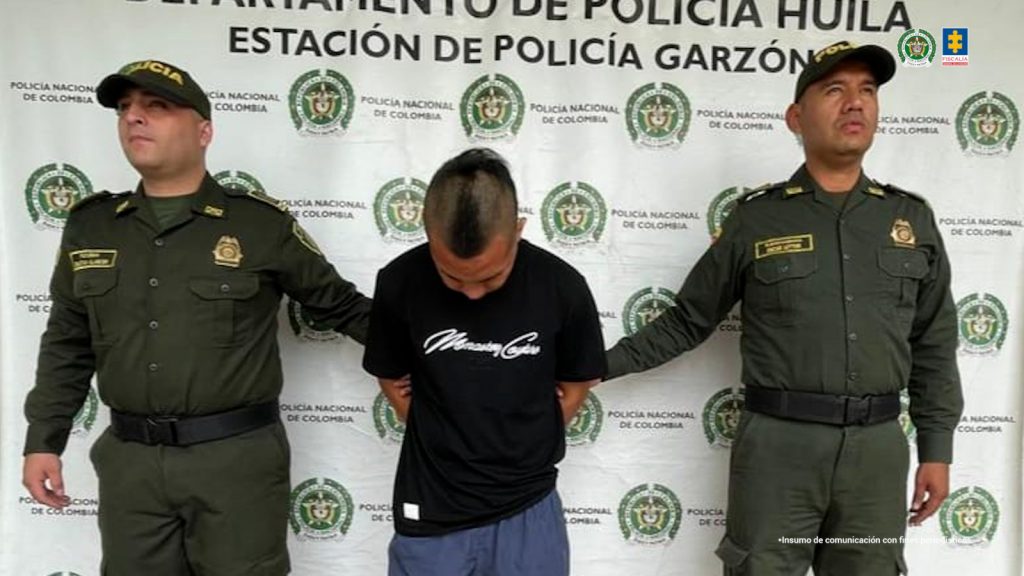 En la foto se observa al agresor quien tiene un buzo negro y unas bermudas azules y se encuentra en custodia por dos uniformados de la Policía Nacional. Detrás hay un backing de la Policía Nacional.