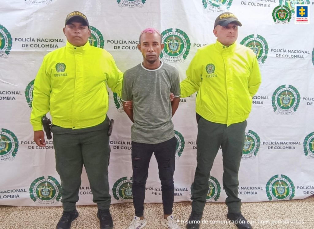 En la fotografía se observan tres personas, dos uniformados de la Policía y el capturado. En la parte posterior se observa un backing con escudos de la Policía Nacional.
