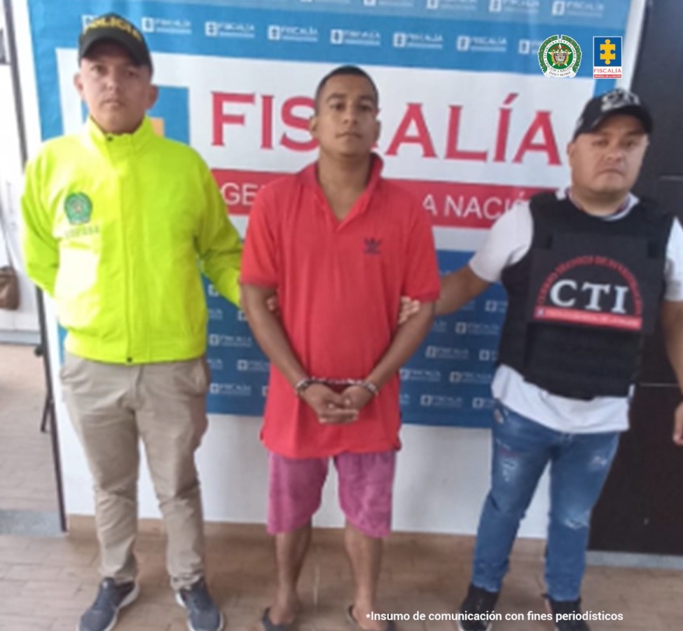 En la fotografía aparece el capturado junto a un servidor del CTI y un agente de la Policía Nacional. En la parte superior se observa un banner de la Fiscalía General