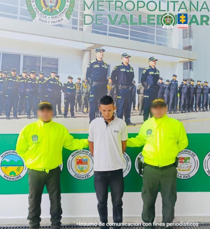 El capturado se encuentra de frente y custodiado por dos uniformados de la Policía Nacional. El capturado tiene un buzo blanco.