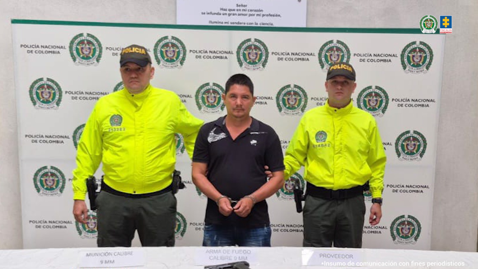 El capturado se encuentra de frente y custodiado por dos uniformados de la Policía Nacional. En la foto se ve de fondo un backing de la Policía Nacional.