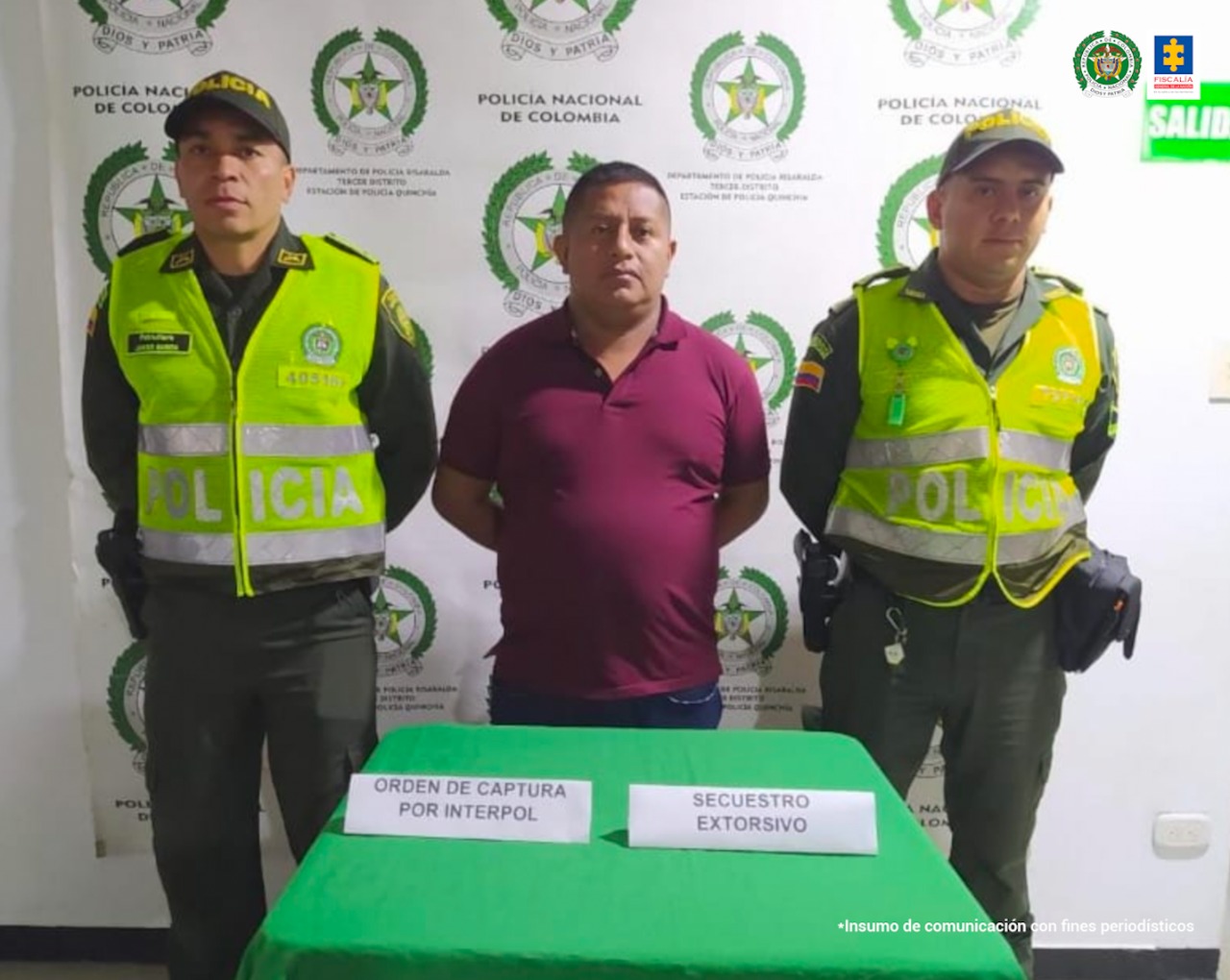 En la foto aparece Ernesto Ascue Boyocue, alias ‘Cuñado’, con los brazos atrás, vestido con camiseta de manga corta color vinotinto y pantalón oscuro. A lado y lado de él hay dos uniformados de la Policía Nacional. Delante de ellos hay una mesa con mantel verde y sobre ella dos letreros que dicen: ‘orden de captura por Interpol’ y ‘secuestro extorsivo’. Detrás de ellos hay un pendón institucional de la Policía.