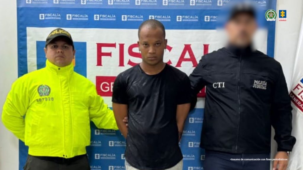 En la fotografía aparece el capturado junto a un servidor del CTI y un agente de la Policía Nacional. En la parte superior está un banner de la Fiscalía General