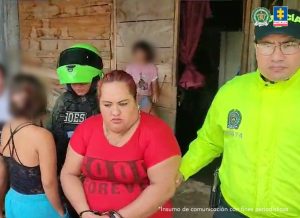 En la foto aparecen la capturada de frente y custodiada por dos uniformados de la Policía Nacional, momentos en que es capturada en cumplimiento a la orden de allanamiento y registro.
