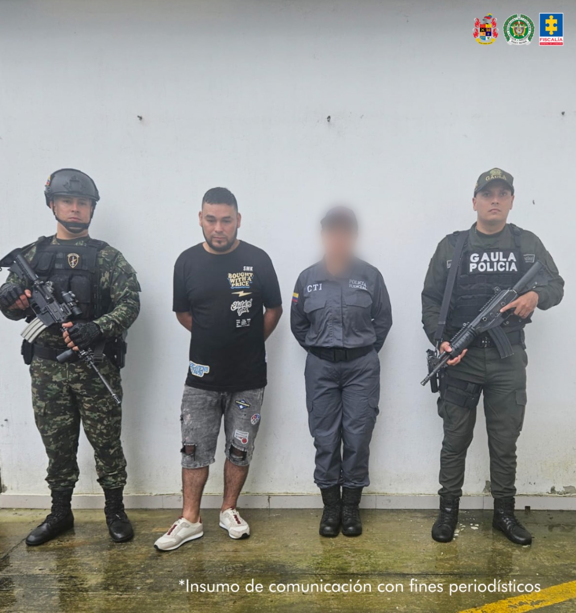El capturado se encuentra de frente custodiado por una servidora del Cuerpo Técnico de Investigación CTI, uniformados del Gaula del Ejército y Policía Nacional.