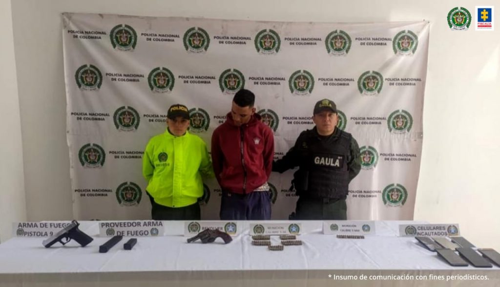 En la fotografía se observan tres personas una de ellas el capturado quien se encuentra sentado en un sofá y dos uniformados de la Policía de pie