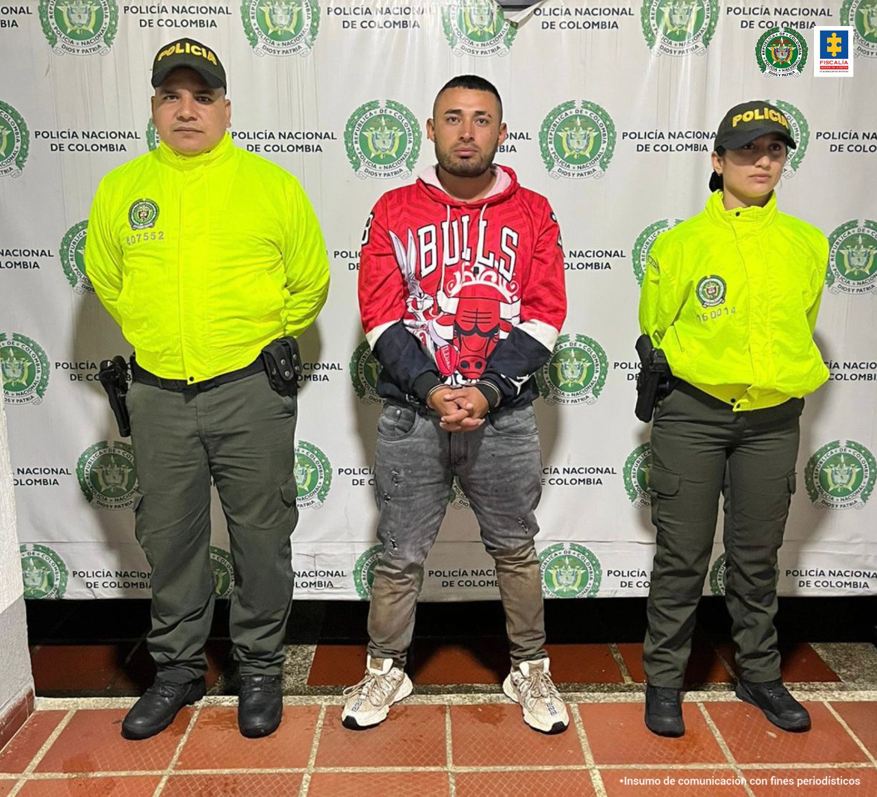 En la fotografía se observan tres personas, una de ellas el capturado y los dos restantes uniformados de la Policía Nacional. En la parte posterior hay un backing de la Policía Nacional.