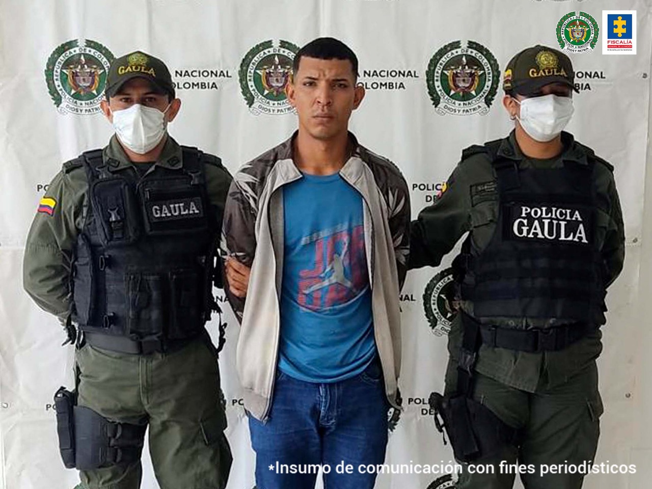En la foto aparece el capturado acompañado de dos uniformados del Gaula de la Policía Nacional. En la parte posterior de la imagen se ve un backing con el logo de la Policía Nacional y se aprecia el logotipo de la Fiscalía General de la Nación.