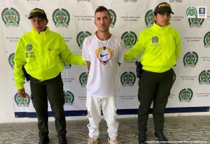 En la fotografía se aprecia de pie y con los brazos atrás a José Walter Salazar López, alias PPK. Viste camiseta blanca con estampado de colores naranja, rojo y negro; así como pantalón claro. A lado y lado de él hay uniformados de la Policía Nacional. Detrás de ellos hay un pendón institucional de la Policía.