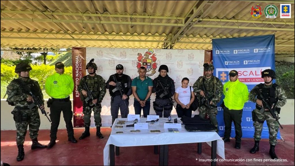 En la fotografía se observan 10 personas dos de ellos los capturados, un hombre y una mujer, cuatro integrantes del Ejército, dos uniformados de la Policía Nacional y dos funcionarios del Cuerpo Técnico de Investigación. En la parte delantera una mesa con elementos incautados y en la parte posterior dos backing del Ejército y de la Fiscalía.