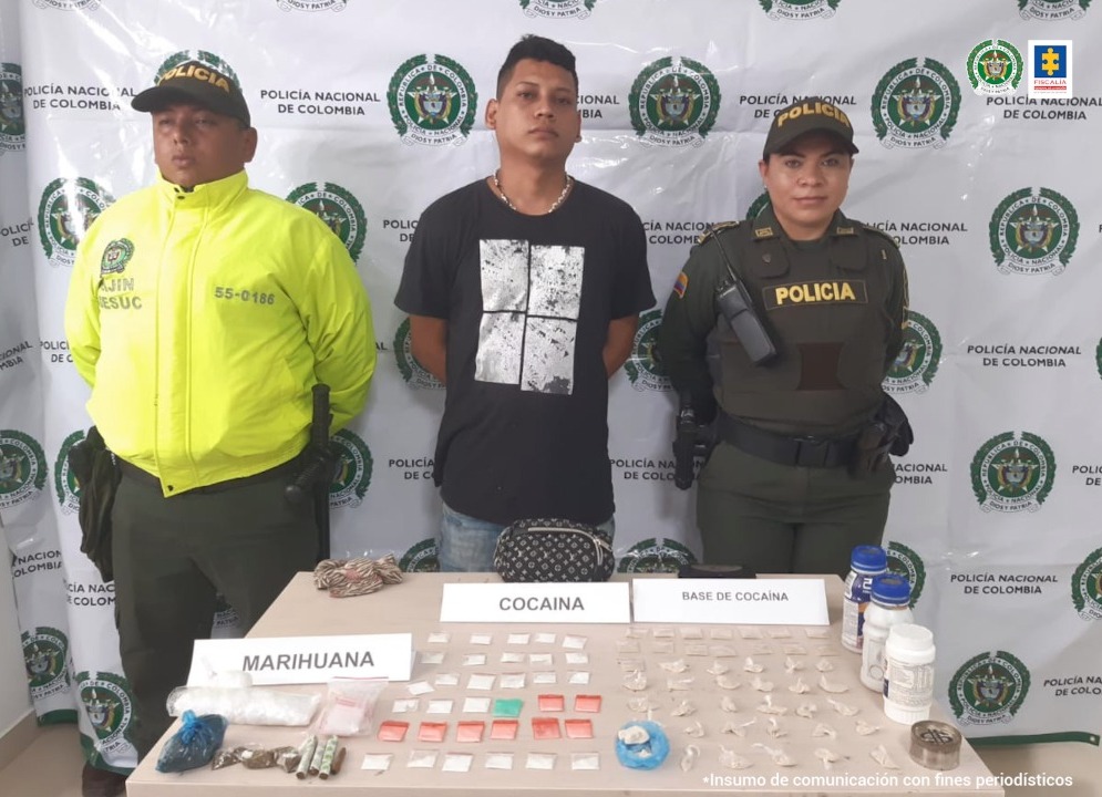 En la imagen se ve un capturado entre dos personas de la Policía frente a una mesa con estupefacientes.