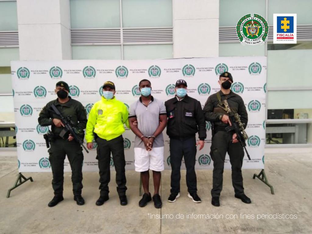 En la fotografía se observan cinco personas, una de ellas el capturado, tres uniformados de la Policía Nacional y un funcionario del Cuerpo Técnico de Investigación (CTI). En la parte posterior se observa un backing de la Policía Nacional.